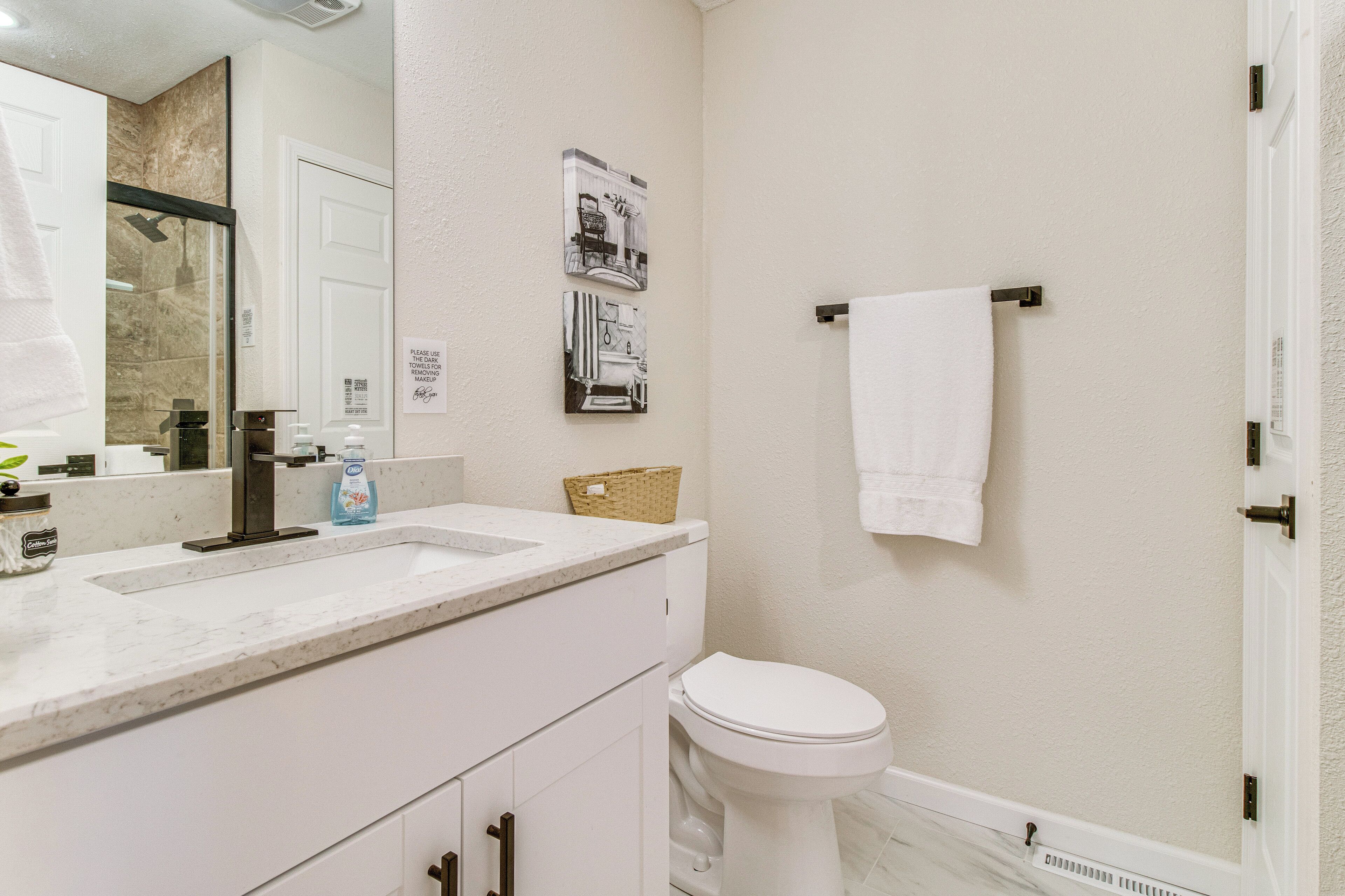 A bathroom with a white sink, a toilet, and a shower. There is a towel hanging on a rack and a basket on the counter.