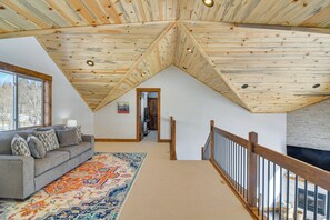 A loft-style room with a sloped ceiling, a gray sofa with patterned cushions, a colorful rug, and a wooden railing. - 'meadowlark Mountain Club' w/ Views of the Rockies (Jefferson)