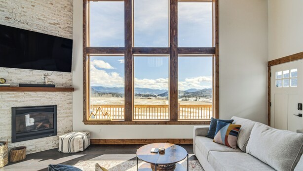 A living room with a fireplace, a large window with a view of mountains, and a cozy seating area.