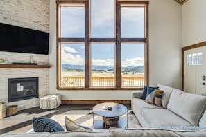 Una sala de estar con chimenea, un ventanal con vistas a las montañas y un rincón de estar acogedor.