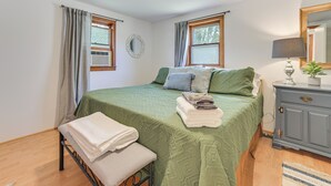 A bedroom with a green bedspread, a bedside table with a lamp, a mirror, and a window with curtains.
