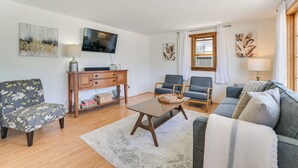 Ein Wohnzimmer mit Sofa, Sesseln, einem Couchtisch, einem Fernseher und Kunstwerken an den Wänden.