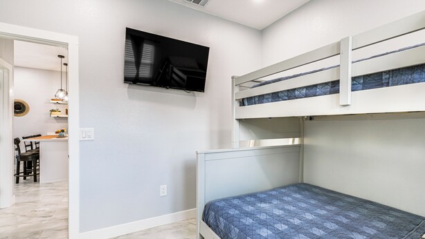 A bedroom with a bunk bed, a flat-screen TV mounted on the wall, and a desk with a chair in the adjacent room. - Small-town Charm & Patio Dining: Home in Madera! (Madera)