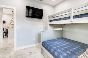 A bedroom with a bunk bed, a flat-screen TV mounted on the wall, and a desk with a chair in the adjacent room. - Small-town Charm & Patio Dining: Home in Madera! (Madera)