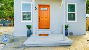 A house with a bright orange front door, white siding, and two potted plants on the porch. - Small-town Charm & Patio Dining: Home in Madera! (Madera)