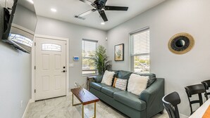 A modern living room with a green sofa, a wooden coffee table, a ceiling fan, and a dining area with chairs. - Small-town Charm & Patio Dining: Home in Madera! (Madera)