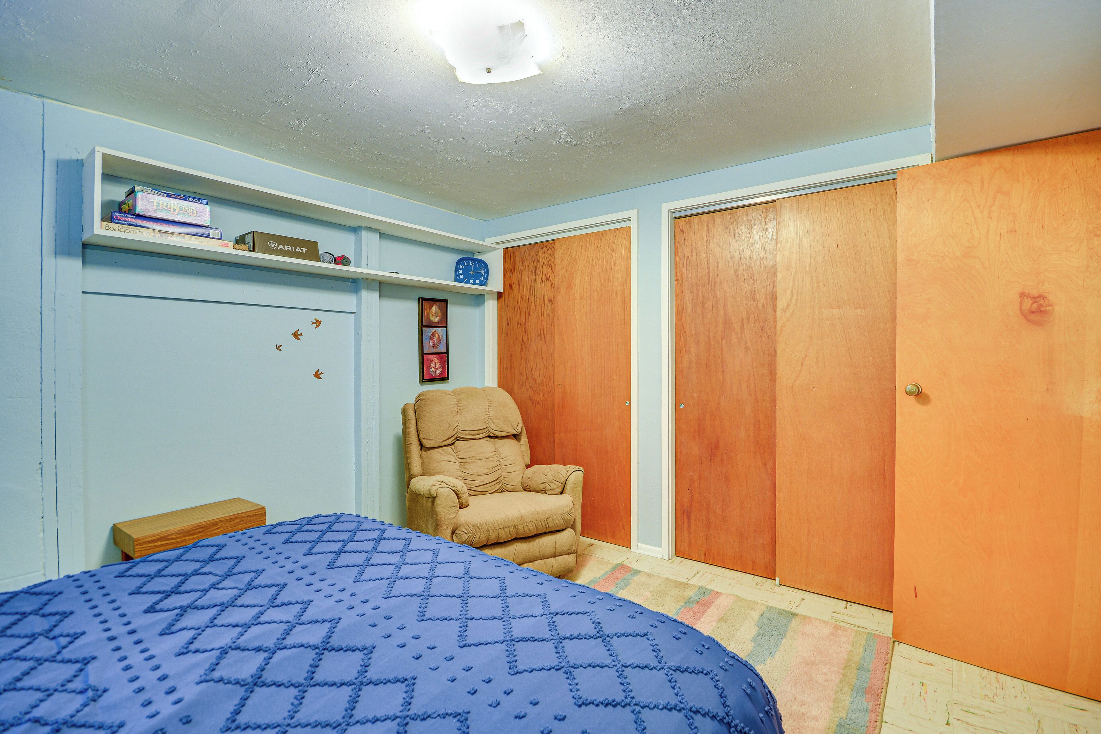 Une chambre à coucher avec un lit, une chaise, une étagère avec des livres, une horloge et une armoire.