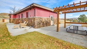 A building with a stone foundation and a red exterior, a wooden pergola, and a picnic table. - 1 Mi to Hot Springs State Park: Rustic Wyoming Gem (Thermopolis)