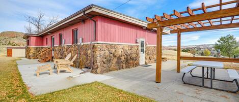 A building with a stone foundation and a red exterior, a wooden pergola, and a picnic table.