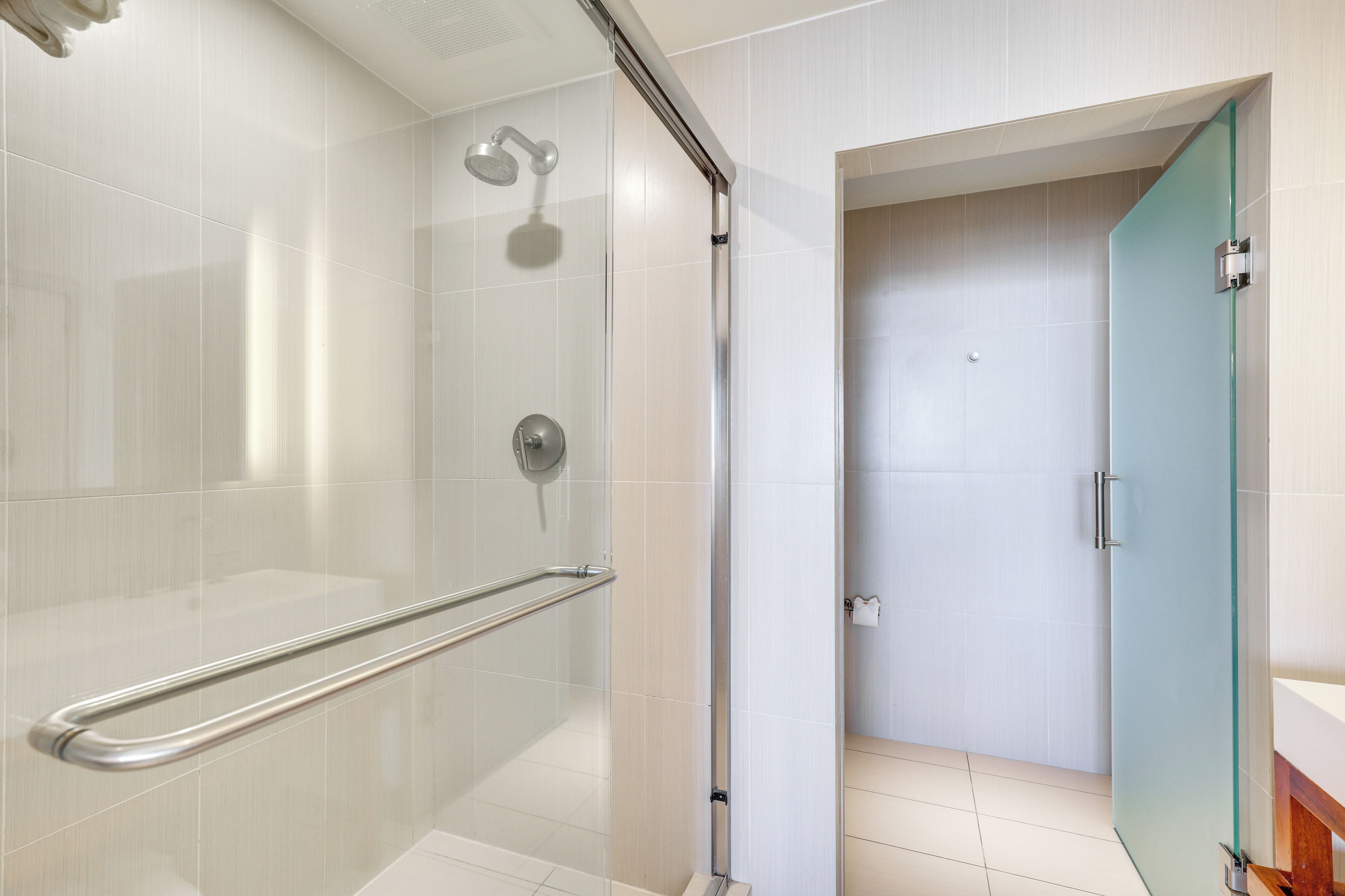 A modern bathroom with a glass shower enclosure, a handrail, and a visible toilet paper dispenser.
