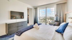 A modern hotel room with a large bed, a flat-screen TV, a view of the city, and a cityscape through the window. - Sleek Fort Lauderdale Condo Near Beaches & Dining! (Fort Lauderdale)