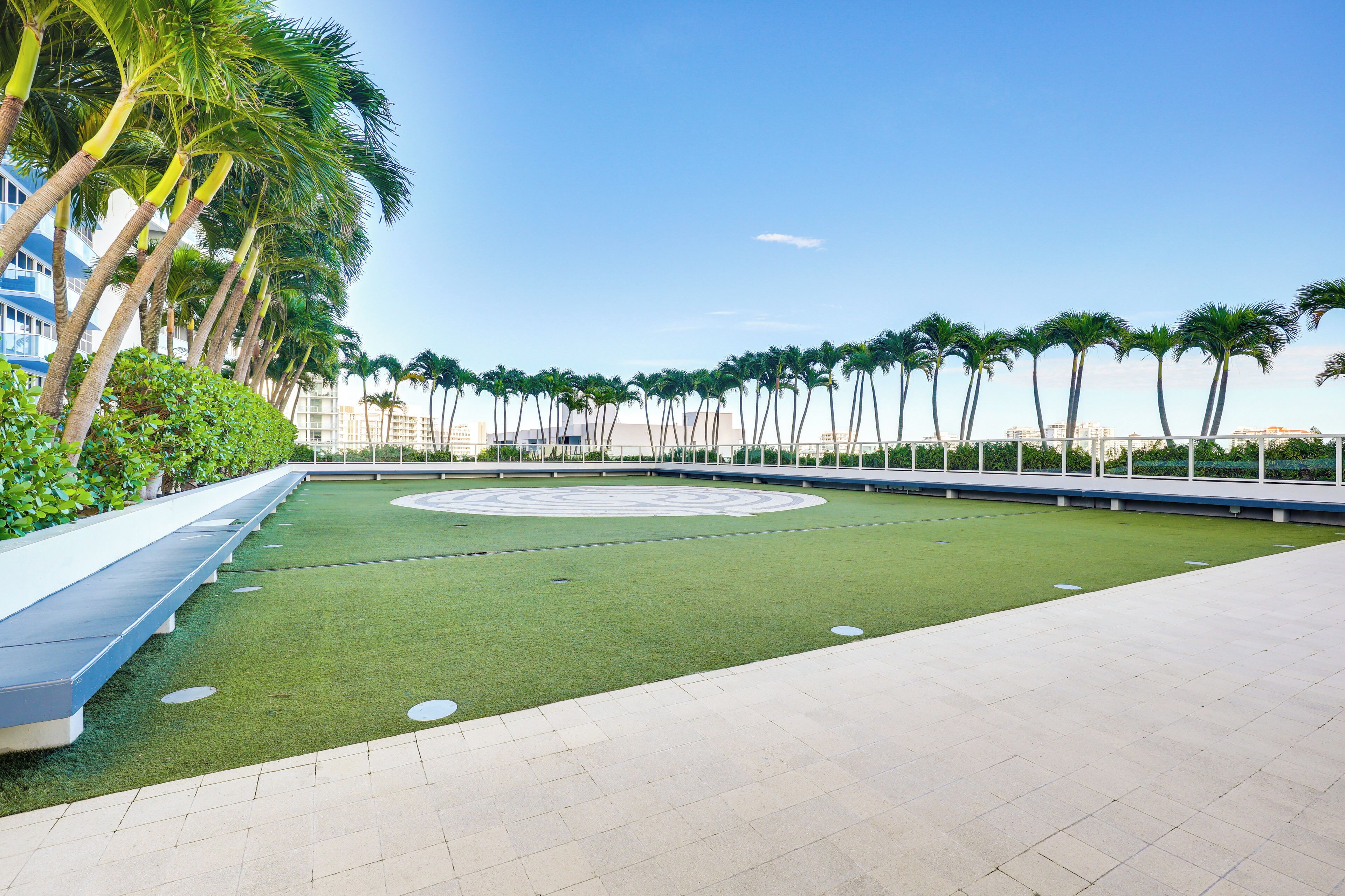 Un área ajardinada con palmeras, un jardín circular y un camino pavimentado.