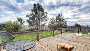 Eine Holzterrasse mit einem Metalltisch und -stühlen, einer Holzbank und Blick auf Bäume und eine ferne Landschaft.