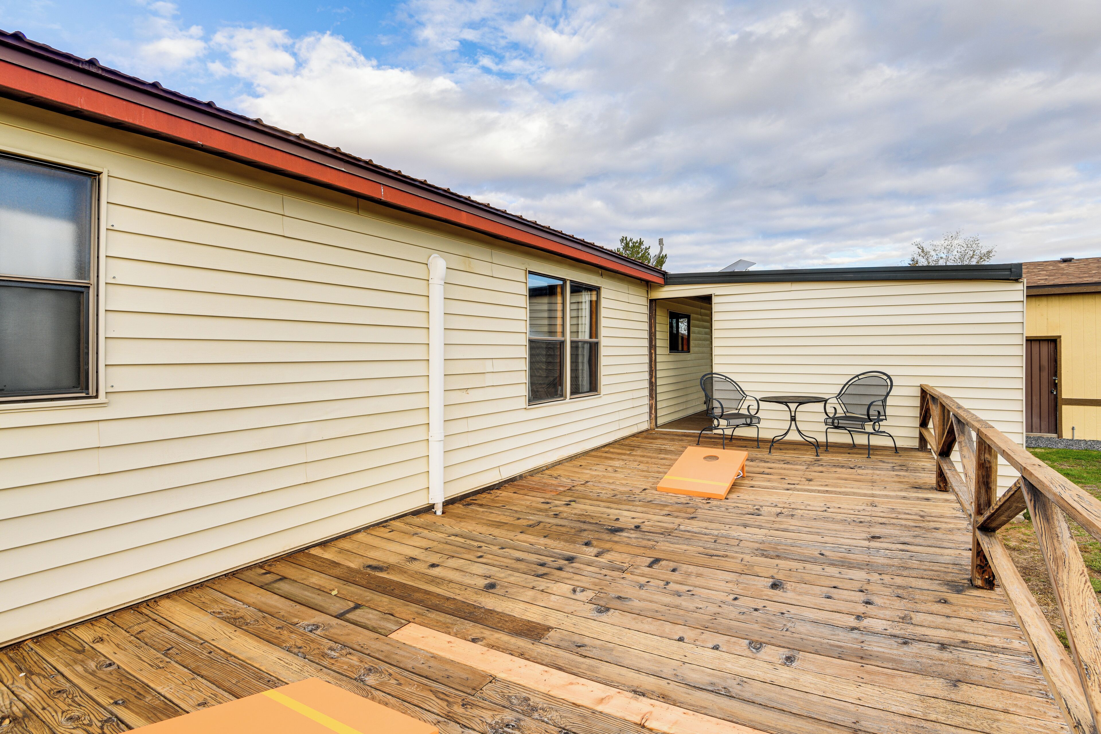 A wooden deck with a metal railing, a table, and two chairs.