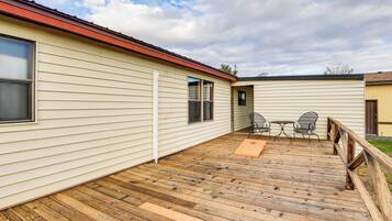 A wooden deck with a metal railing, a table, and two chairs.