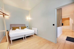 Cozy retreat with a neatly made bed, bedside table, and radiator, set against light-colored walls and wooden flooring.