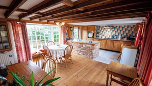 A kitchen with wooden cabinets, a central island, and a dining area with wooden chairs and a table. - Cosy converted barn in rural location with views of the surrounding countryside. (Newport)