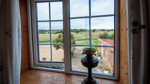 A room with a large window, a wooden floor, and a table lamp. - Cosy converted barn in rural location with views of the surrounding countryside. (Newport)