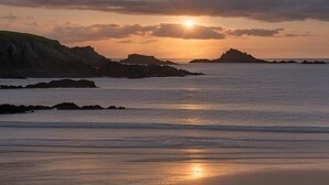 A coastal sunset with rocky outcrops and calm sea. - Dwylan : Spacious Family Home Near Rhosneigr Beach | Managed by Anglesey Holiday Lettings (Rhosneigr)