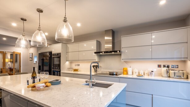 A modern kitchen with white cabinetry, a marble countertop, and pendant lighting. - Dwylan : Spacious Family Home Near Rhosneigr Beach | Managed by Anglesey Holiday Lettings (Rhosneigr)