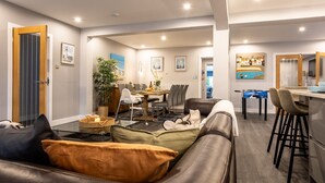 A modern living room with a sofa, a dining area with a table and chairs, and a kitchen area with bar stools. - Dwylan : Spacious Family Home Near Rhosneigr Beach | Managed by Anglesey Holiday Lettings (Rhosneigr)
