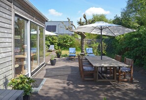 An outdoor patio with a wooden table and chairs, a large umbrella, and a glass door leading to a room. - Vacation home MV8 (Egmond-Binnen)