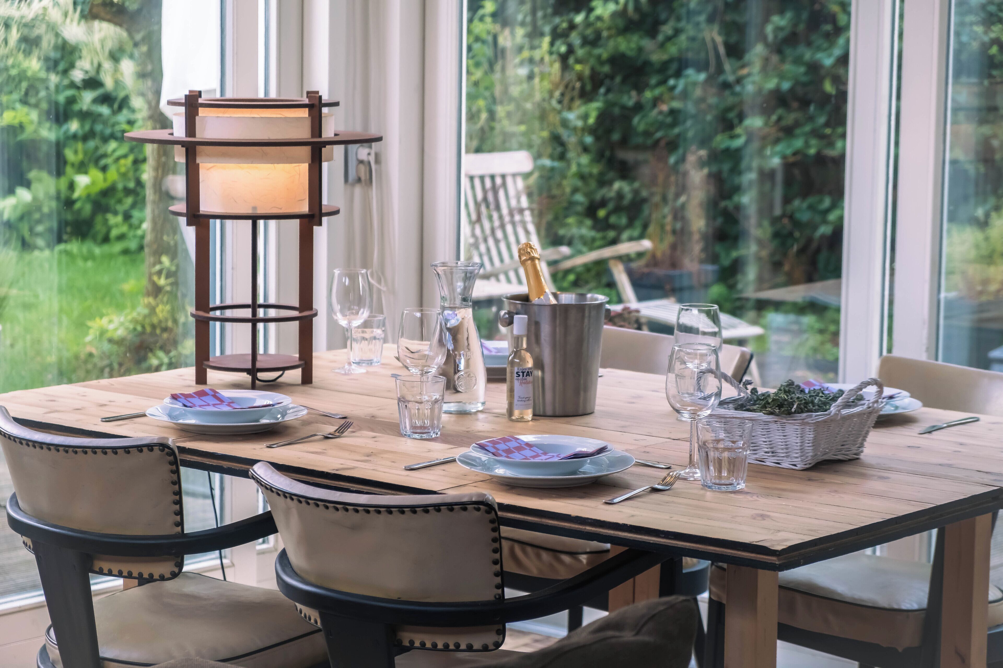 A wooden dining table set with plates, glasses, a bottle of champagne, and a candle holder.