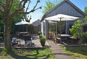 A wooden deck with outdoor furniture, a potted plant, and a building with large windows. - Vacation home MV8 (Egmond-Binnen)