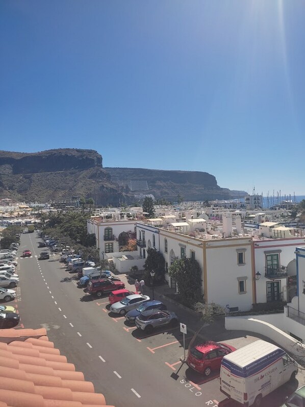 A parking lot with cars and a truck, buildings with balconies, and a clear sky. - Paraiso 9 by El Sirocco (Mogan)