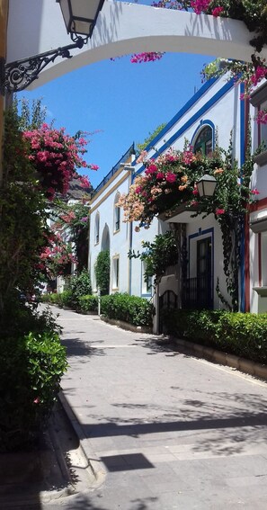 A narrow street with buildings on either side, some with balconies and flower boxes. - Paraiso 9 by El Sirocco (Mogan)