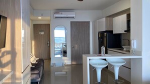 A modern kitchen with white cabinets, a black refrigerator, and a white countertop. There is a ceiling fan, an air conditioning unit, and a view through an arched doorway. - w Divine Loft w Ocean View in Crespo (Cartagena)