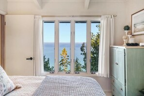 A bedroom with a large window, a bed, a dresser, and a door.