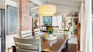 A dining area with a long wooden table, chairs, a hanging light fixture, and a brick column.