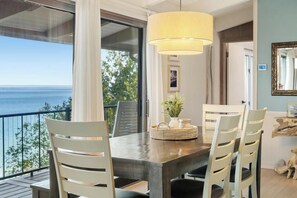 A dining area with a table, chairs, a hanging lamp, and a view of the sea.