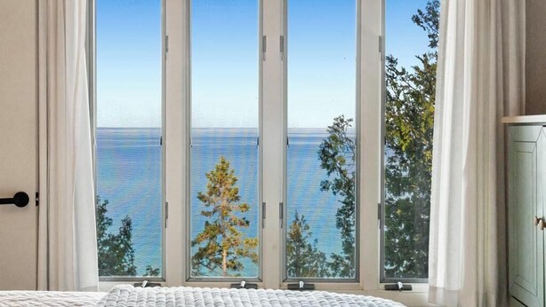 A room with a large window overlooking the sea, a bed, and a cabinet.