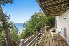 A wooden deck with a rocking chair, overlooking a body of water and dense greenery.