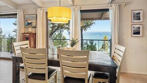 A dining area with a table, chairs, a yellow pendant light, and a view of the sea through large windows.