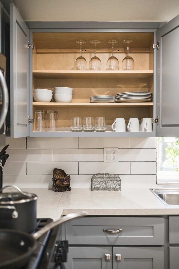 A kitchen with a wooden cabinet containing bowls, plates, glasses, and a wine glass holder. - Charming Escape With Stylish Decor Outdoor Space (Glendora)