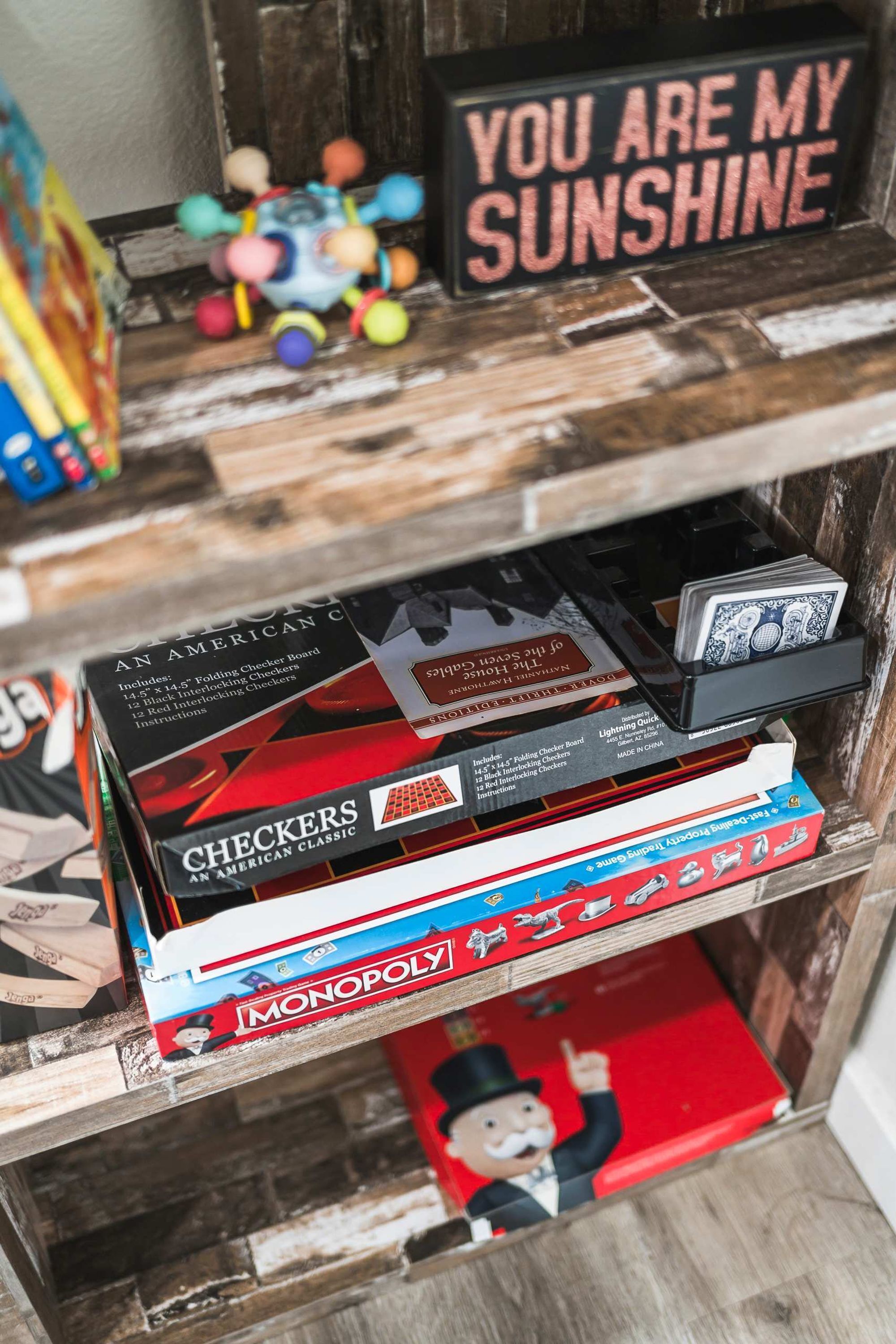 A shelf with various board games including Checkers, Monopoly, and a sign that says "You are my sunshine".