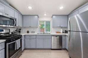 A modern kitchen with grey cabinets, stainless steel appliances, and a window with a view of greenery. - Charming Escape With Stylish Decor Outdoor Space (Glendora)