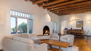A modern living room with a fireplace, white sofas, a wooden coffee table, and a dining area with a table and chairs. - Sunset Mountain Ranch - 5 Bedroom (Santa Fe)