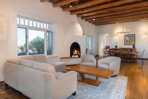 A modern living room with a fireplace, white sofas, a wooden coffee table, and a dining area with a table and chairs.