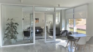 Een modern interieur met een glazen wand, een eethoek met tafel en stoelen, en uitzicht op een fietser buiten.