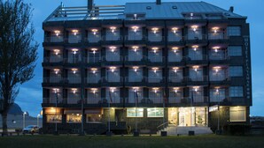 Een hotel met meerdere verdiepingen, balkons, een geparkeerde auto ervoor en een goed verlichte ingang.