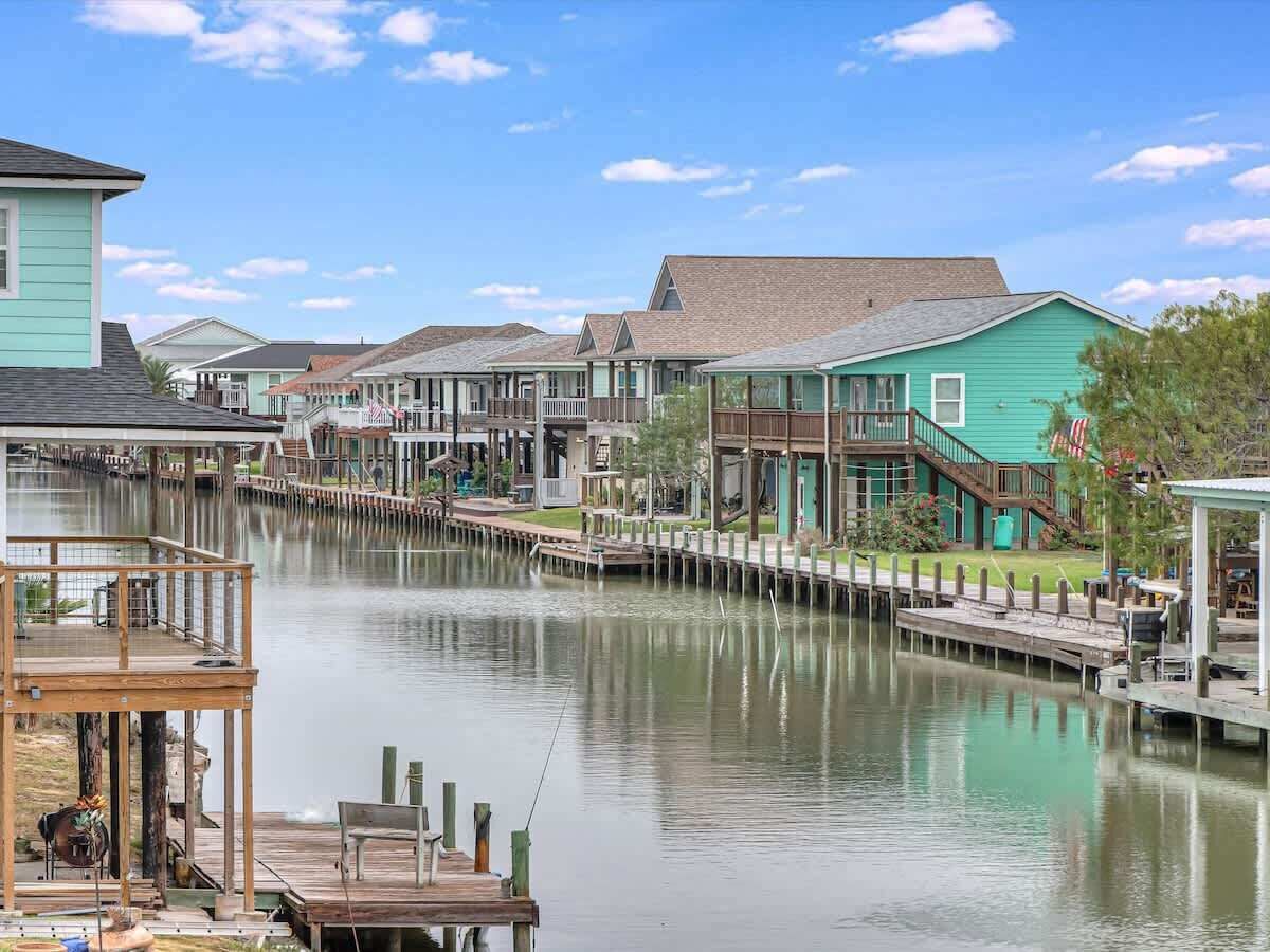 Een pand aan het water met aangemeerde boten, een houten terras en een rij huizen met een pier die het water in reikt.