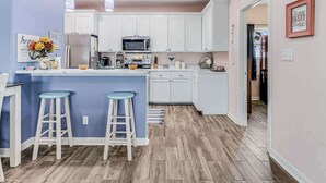 A kitchen with white cabinets, a blue island with stools, a microwave, and a sink. - Twin Palms 2.0 (Rockport)