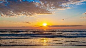Ein Sonnenuntergang über dem Meer, Wellen nähern sich dem Ufer.