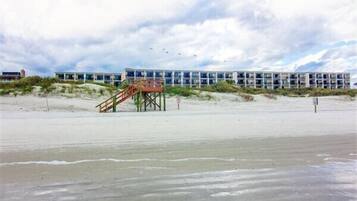 Een hotel aan het strand met een trap naar een toegangspunt tot het strand, een zandstrand en een gebouw met meerdere verdiepingen.