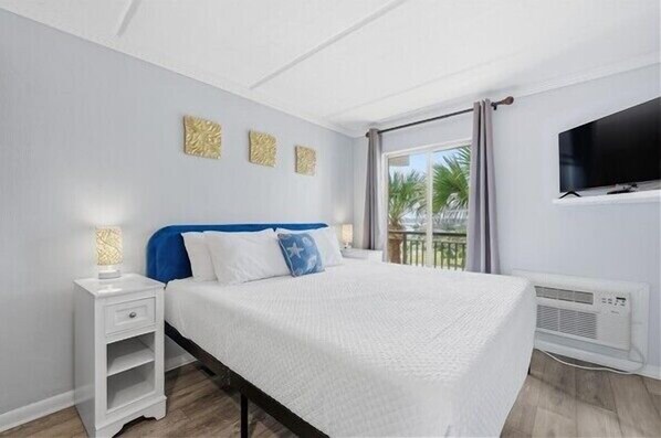 A bedroom with a bed, a nightstand, a TV, and a window with curtains.