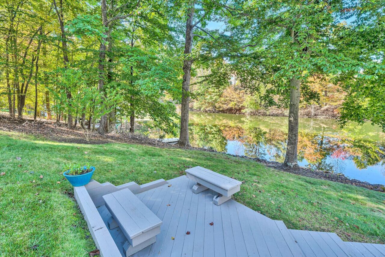 A wooden deck with benches and a planter, surrounded by trees and a body of water.